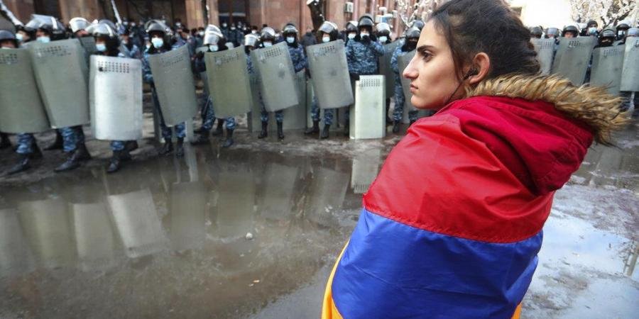 A woman wearing a state Armenian flag stands in front of a riot police line during a rally to pressure PM Nikol Pashinyan to resign over a peace deal with neighboring Azerbaijan.